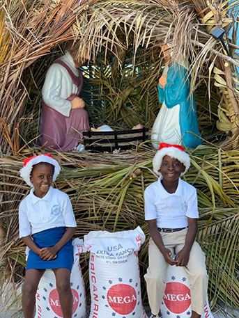 two kids wearing Santa hats sitting on sacks of rice