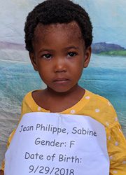 A young girl holding a sign that says jean philippe sabine gender f date of birth.