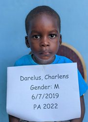 A young boy holding up a sign that says darel charles gender m.