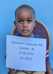 A young boy holding up a sign that reads dorsali guyane ally gender m.