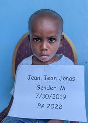 A young boy holding a sign that says jean jonas gender m.