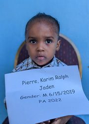 A young boy holding a sign that says pierre karm raphael jaden.
