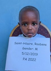 A young boy holding up a sign that says saint hilaire roberts gender.